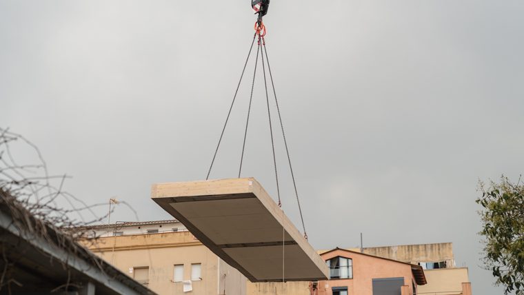 Una grua col·loca una de les peces de fusta de l'estructura de l'ampliació de l'escola bresso municipal La Mar